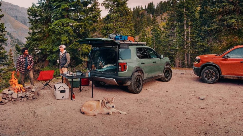Two people and a dog sitting outside next to a fire and two parked 2026 Honda Passports.